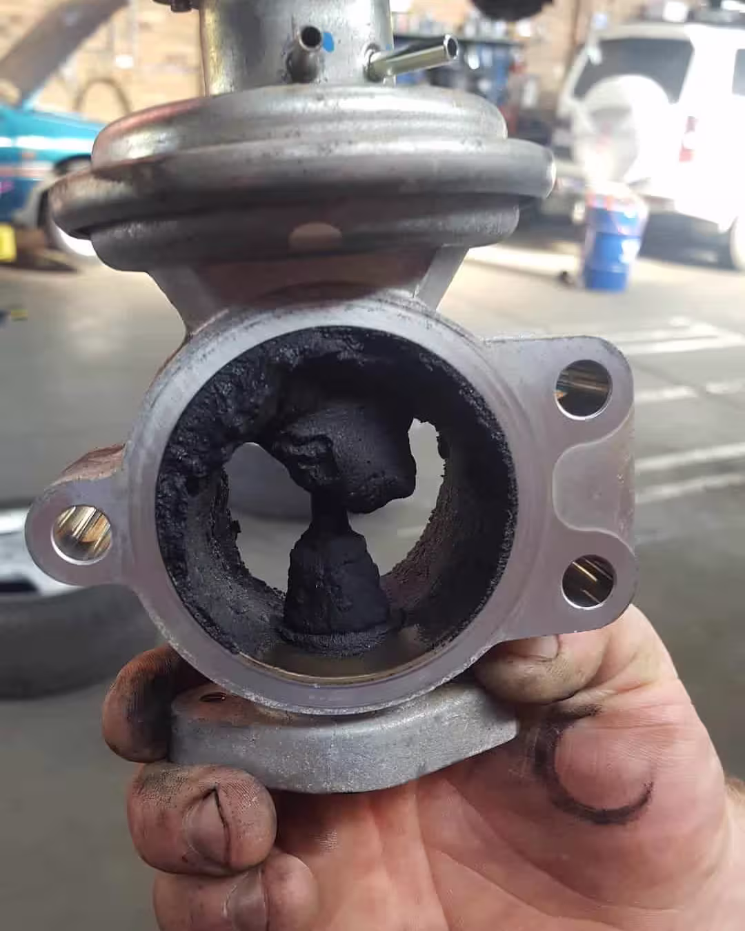 EGR valve held in a mechanic's hand, the bore almost closed off by a plug of carbon around the valve stem