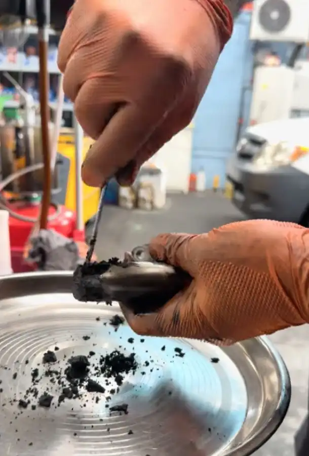 Nas scraping baked carbon off an EGR valve by hand over a tray at the Kings Park workshop