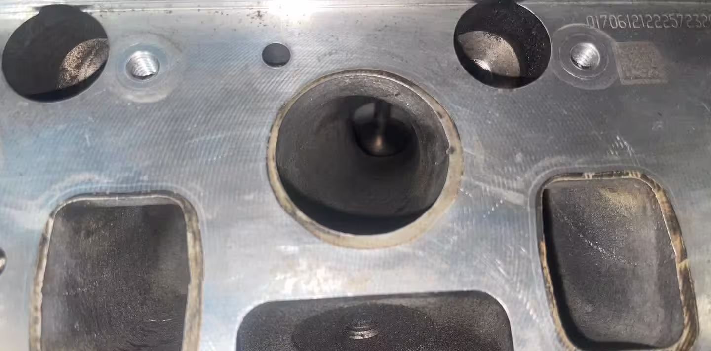 The same cylinder head intake face after cleaning, bare metal with the valve visible in the port